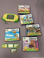 Leapster Explorer handheld console in green and yellow alongside 5 game boxes and 5 game cartridges laid out on a cloth surface.