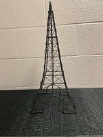 Front view of the black metal Eiffel Tower sculpture, showing lattice framework and arch details at the base.