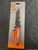 Photo of ParaKnife 4.0 FS para-cutter knife in sealed package showing orange handle with lanyard and sawtooth blade design