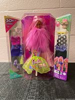 Full view of Barbie Extra doll in packaging with pink fur, long pink hair, neon green skirt and accessory sets on sides