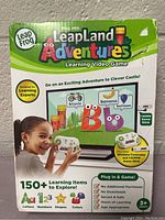 Photo of the front box showing Leap Frog LeapLand Adventures Learning Video Game with colorful letters and objects on screen, child holding wireless controller.