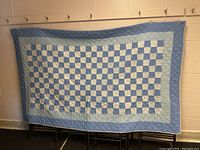 Front view of large quilt with blue and white checkerboard patchwork hung against wall.