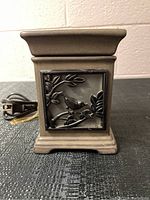 Front view of square brown ceramic Scentsy wax melter with metal inset featuring bird and leaves on branches, electrical cord visible.