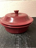 Side angle view of cranberry round covered stoneware baker, showing the lid and knob handle.