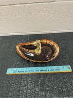 Side view of the ceramic ashtray with brass bowling figurine and ruler for scale.