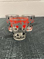 Three glass tumblers with playing card suits printed in red and black, showing pattern of hearts, diamonds, clubs, and spades.