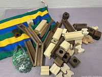 Wooden marble run pieces scattered on a surface with multi-colored striped fabric bag beneath