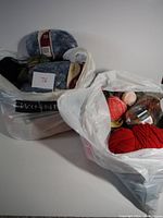 Two large white plastic bags filled with various colored wool yarn skeins, some with original packaging visible.