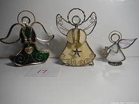 Three stained glass angel figurines including two larger candle holders in green and yellow with detailed metal wire frames and one smaller iridescent angel holding a teddy bear