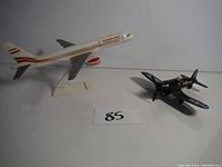 Photo shows two airplane replica models on a surface, one commercial airplane on a stand and one black military airplane.