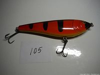 Photo showing full side profile of the 7 inch fishing lure with orange, black, and yellow coloring and attached treble hooks.