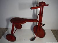 Side view of antique red tricycle showing wooden seat with damage and metal frame.