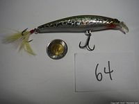 Silver/gray Cultiva jerkbait lure with feathered tail and 2 treble hooks next to a coin for scale and lot number