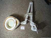 Magnifying light with adjustable arm laid out on carpet showing full length and cord.