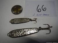 Two hammered silver slab fishing spoons with treble hooks and loops for line attachment, placed next to a coin and a handwritten note indicating the lot number and item count.