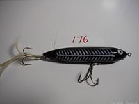 Side view of the topwater lure showing black body with white skeletal design and feathered treble hook
