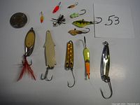 Wide shot showing all ten ice fishing lures arranged on a white surface next to a coin for scale.