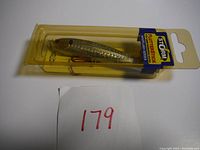 Side and top view of new, unopened Storm Flutterstick fishing lure in yellowed packaging showing branding and treble hooks.