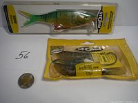 Photo showing Storm Kick'n Minnow hard bait in blister packaging next to Wiley Buzz'n Tail Shad soft baits in sealed bag, coin for scale.