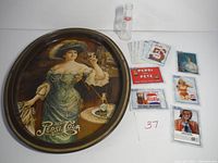 Photo showing the round vintage Pepsi Cola metal tray with artwork of a woman holding a glass of Pepsi, the mini bottle behind it, and several collectible cards spread near the tray.
