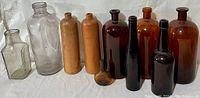 Full view of the group of antique bottles including clear glass, ceramic, and brown glass bottles of various shapes and sizes.