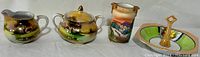 Full view of all four pieces in the set: creamer, sugar bowl, vase, and tidbit plate showing painted scenes.