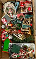 Overhead view of a large box filled with assorted vintage Christmas decorations including ornaments, figurines, greenery, and miniature decorations.