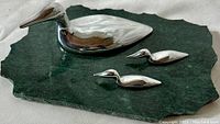 Front and top view of three aluminum duck sculptures on dark green marble base.