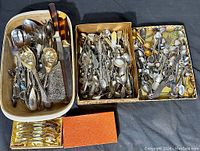 Overview of the lot showing three containers filled with a large variety of spoons, serving pieces, and knives.