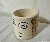 Side view showing stylized face drawing on pottery cup with black outlines and brown brushstroke accents.