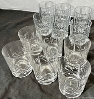 Photo showing both sets of clear cut crystal tumblers arranged on a dark surface; front set features floral/starburst cut design with vertical facets.