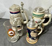 Photo showing four vintage beer steins with hinged lids and one glass beer mug with Canadian Forces crest, displayed on cloth background.