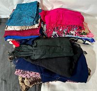 Top view photo showing piles of assorted scarves of various colors including bright pink, dark blue, black, and patterns such as snakeskin and animal prints.