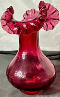 Side view of the cranberry glass vase showing its bulbous body and flared, ruffled edge on top.
