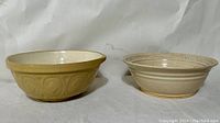 Two vintage pottery mixing bowls side by side, one beige with diamond pattern and one cream colored with decorative rim