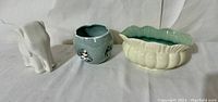 Three vintage pottery planters in a row on white surface: white elephant planter, small cubist textured planter with floral, cream scalloped planter
