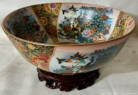 Side angled view of the Satsuma porcelain bowl showing hand-painted birds and floral decorations with wood plinth base underneath.