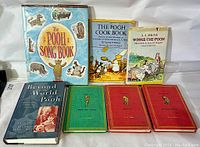 Front view of the seven books showing spines and cover art including 'The Pooh Song Book', 'The Pooh Cook Book', and 'Winnie-the-Pooh' with classic Pooh illustrations
