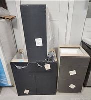 Three base cabinets stacked and displayed; two cabinets with doors and one with drawers, wrapped and tagged.