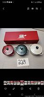 Three petite round Le Creuset casseroles displayed next to their original box, showing red, green, and white colors with lids and black knobs.