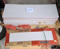 Stack of white ceramic tiles in damaged Emigres box with label '204'