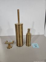 Photo of the gold plated towel hook, soap dispenser, and brush holder with brush arranged side by side on a white background.