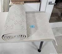 Rolled and unrolled view of the white carpet runner showing full width and rolled length on a table.