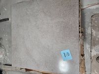 Close-up of a single light gray ceramic tile showing texture and finish, with lot label 127 visible.