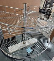 Photo showing two-tier kidney-shaped lazy Susan shelves with chrome wire construction and central support pole.