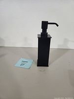 Front view of the black metal soap dispenser with pump attached.