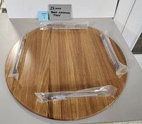 Top-down photo showing the circular wooden tray with three metal handles wrapped in plastic and laid out on the tray.