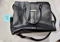 Black Danier leather purse with textured front panel, dual handles, adjustable shoulder strap, and gold-tone accent on central strap closure. Six metal feet on base. Very clean condition.