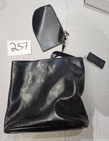 Black textured purse with handles alongside matching black clutch, both with tags and functional zippers.