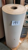 Vertical view of a large roll of masking paper standing upright, showing the outer surface and size relative to surrounding buckets.